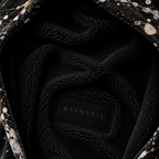 Close-up of a black plush fleece-lined interior with a black label reading RAVNVEIL in gold lettering, surrounded by a black fabric with white and gold speckled pattern.