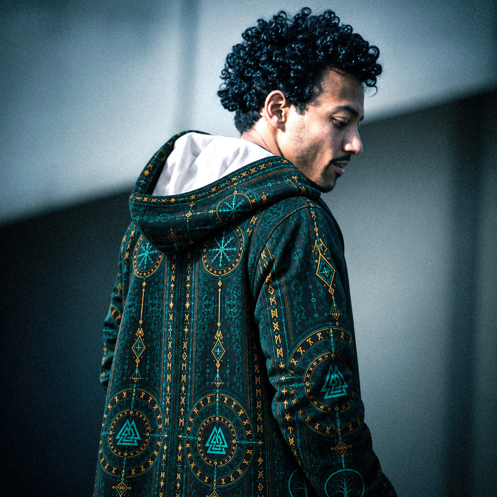 RuneBloom Eternal Cloak featuring an intricate teal and gold rune pattern with Valknut-inspired symbols, shown from the back with a white-lined hood in a moody urban setting.
