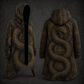 A hooded longline coat shown from the front and back on a dark studio background. The garment has an all-over intricate serpent and circular geometric pattern in warm gold and brown tones on a black base.